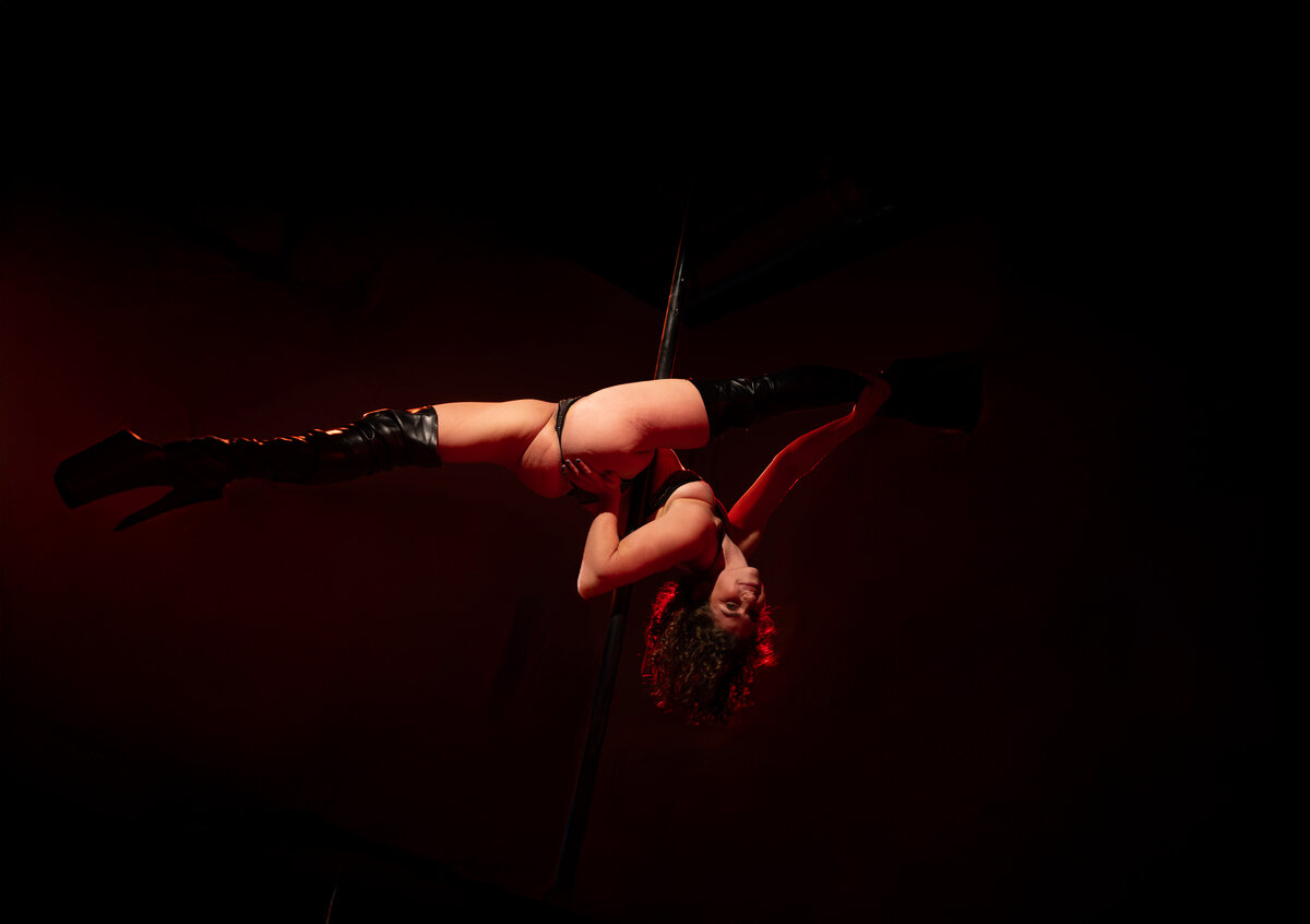Sara inverted on pole with dramatic red lighting